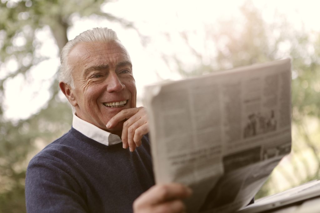 Man holding newspaper while sitting out side smiling reading about PVI in newspaper