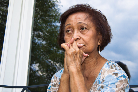 Woman sitting in front of window with hands clasped in front of her mouth.