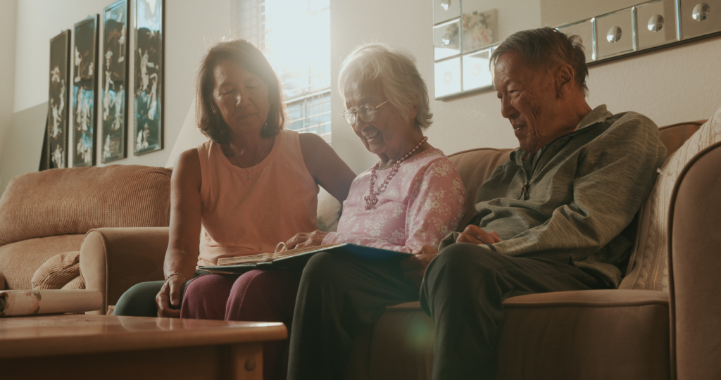 Three people sit on a couch looking at a photo book.